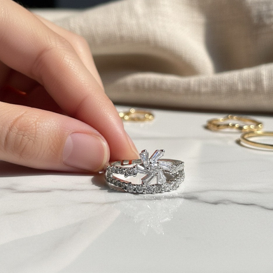 Silver ring with diamond accents held by a hand on a white surface with other rings in the background.