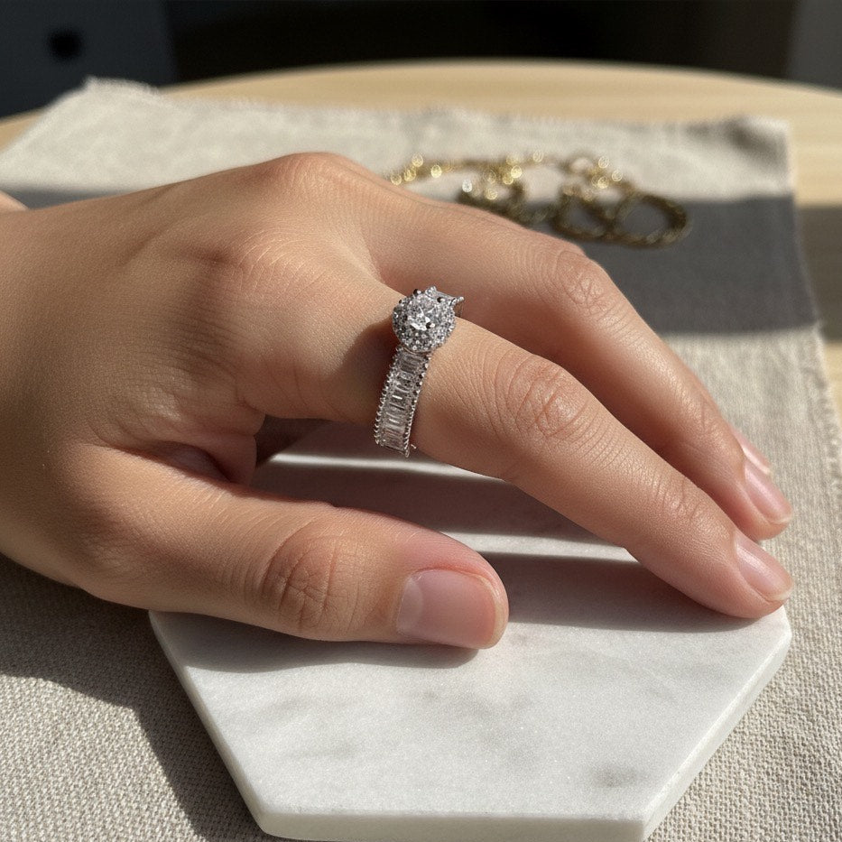 Hand wearing a silver ring with a large diamond on a marble stand.