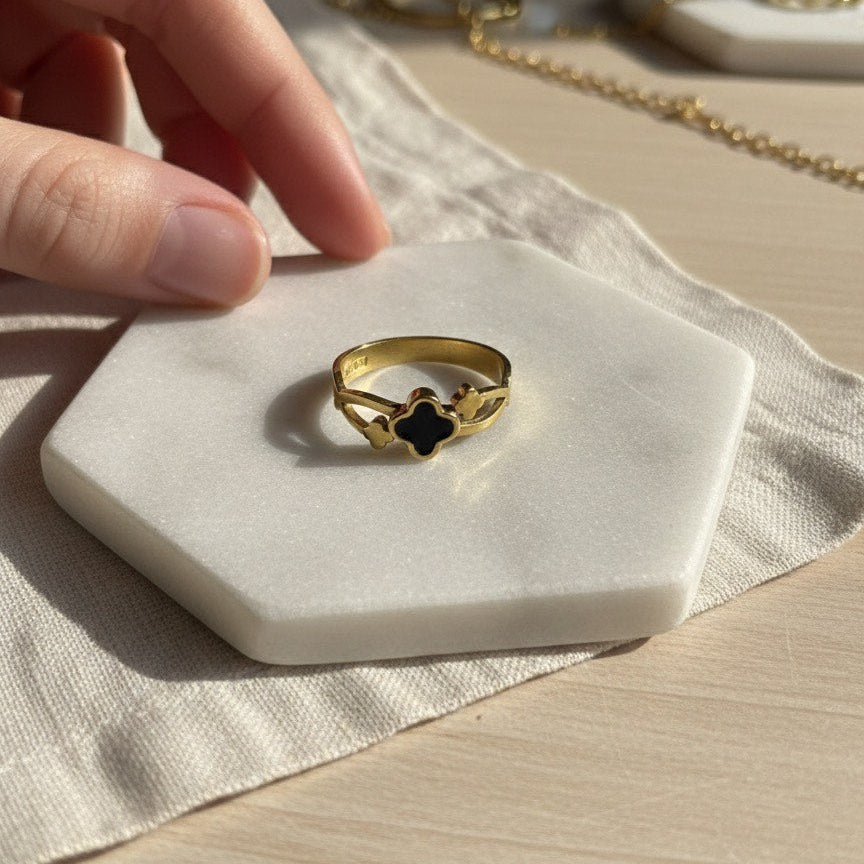 Gold ring with a black center on a white stone surface, with a hand reaching towards it.