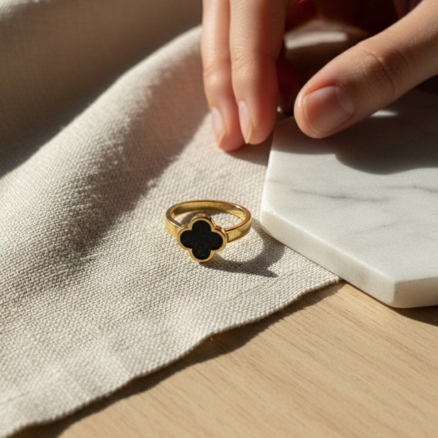 Gold ring with a black clover design on a beige fabric surface