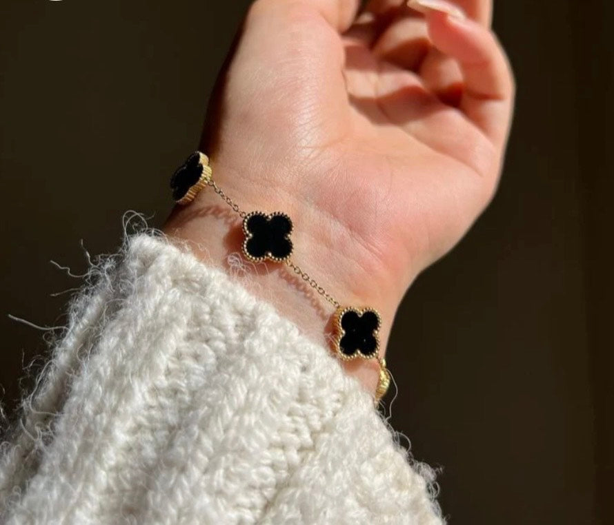 Bracelet with black clover-shaped charms on a wrist against a dark background