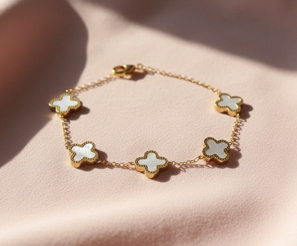 Gold bracelet with white flower-shaped charms on a pink surface