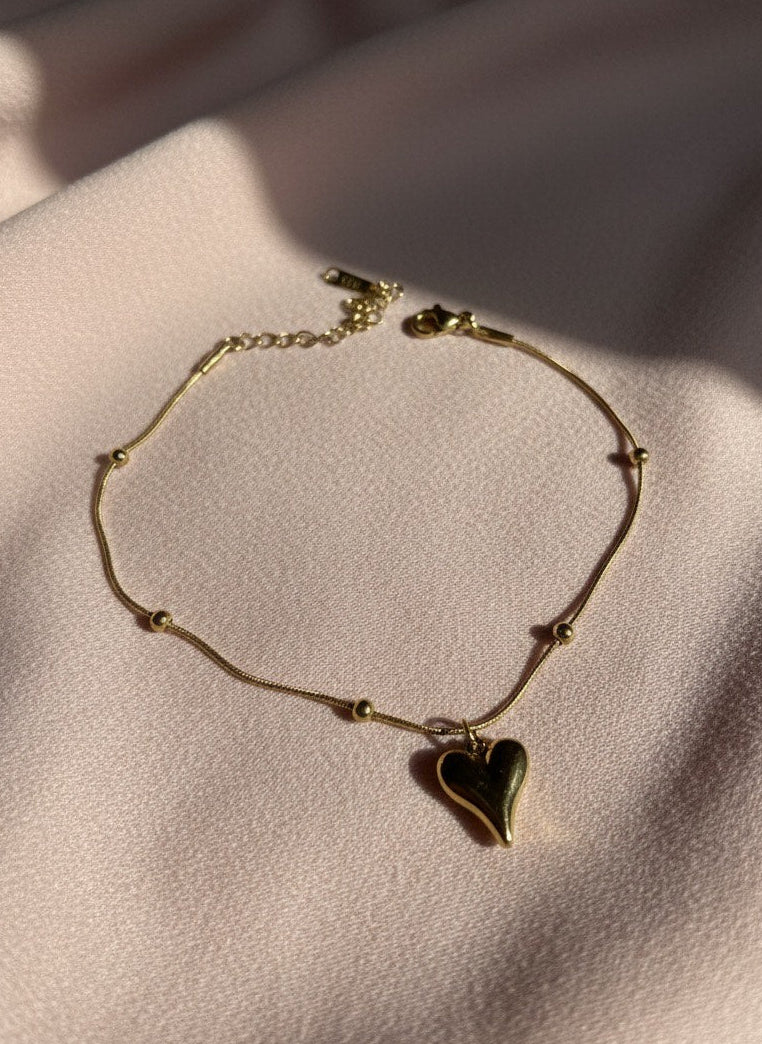 Gold bracelet with a heart charm on a soft pink fabric background