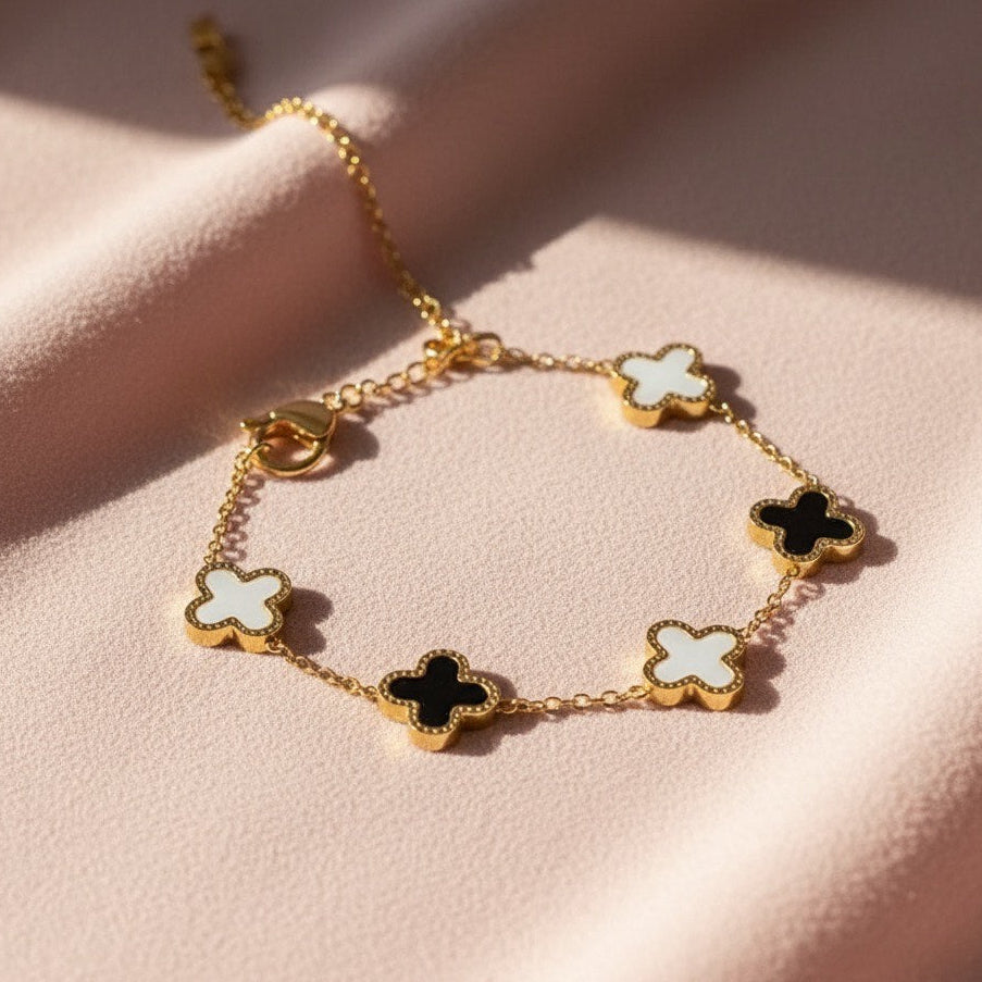 Gold bracelet with clover-shaped charms on a pink surface