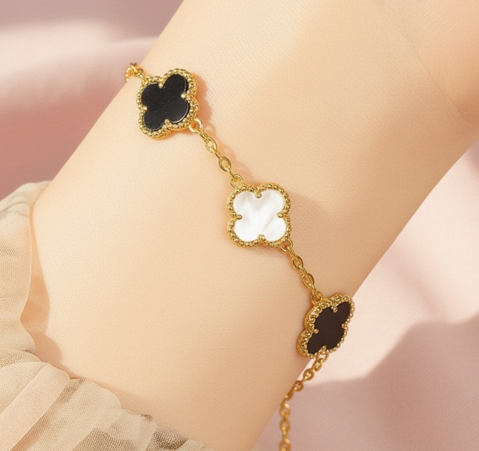 Gold bracelet with black and white clover-shaped charms on a wrist against a pink background