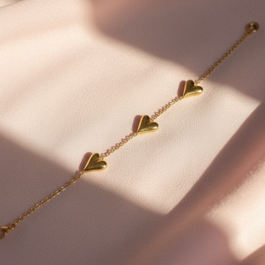 Gold bracelet with heart-shaped charms on a soft pink background