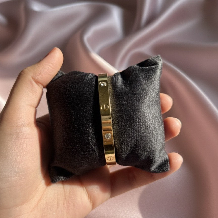 Gold bracelet with a diamond on a black velvet pillow held in a hand against a pink satin background
