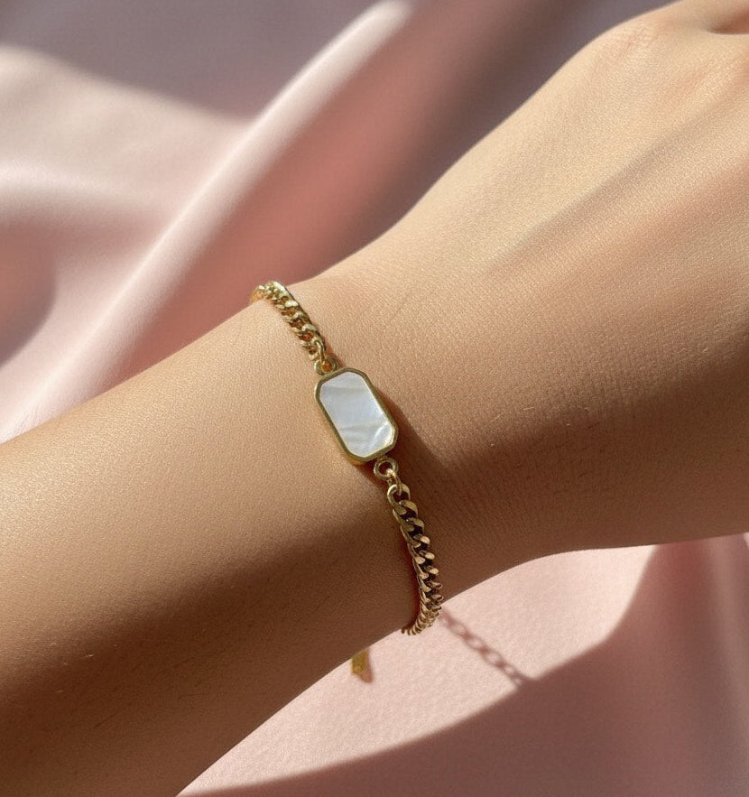 Gold bracelet with a rectangular gemstone on a wrist against a pink fabric background