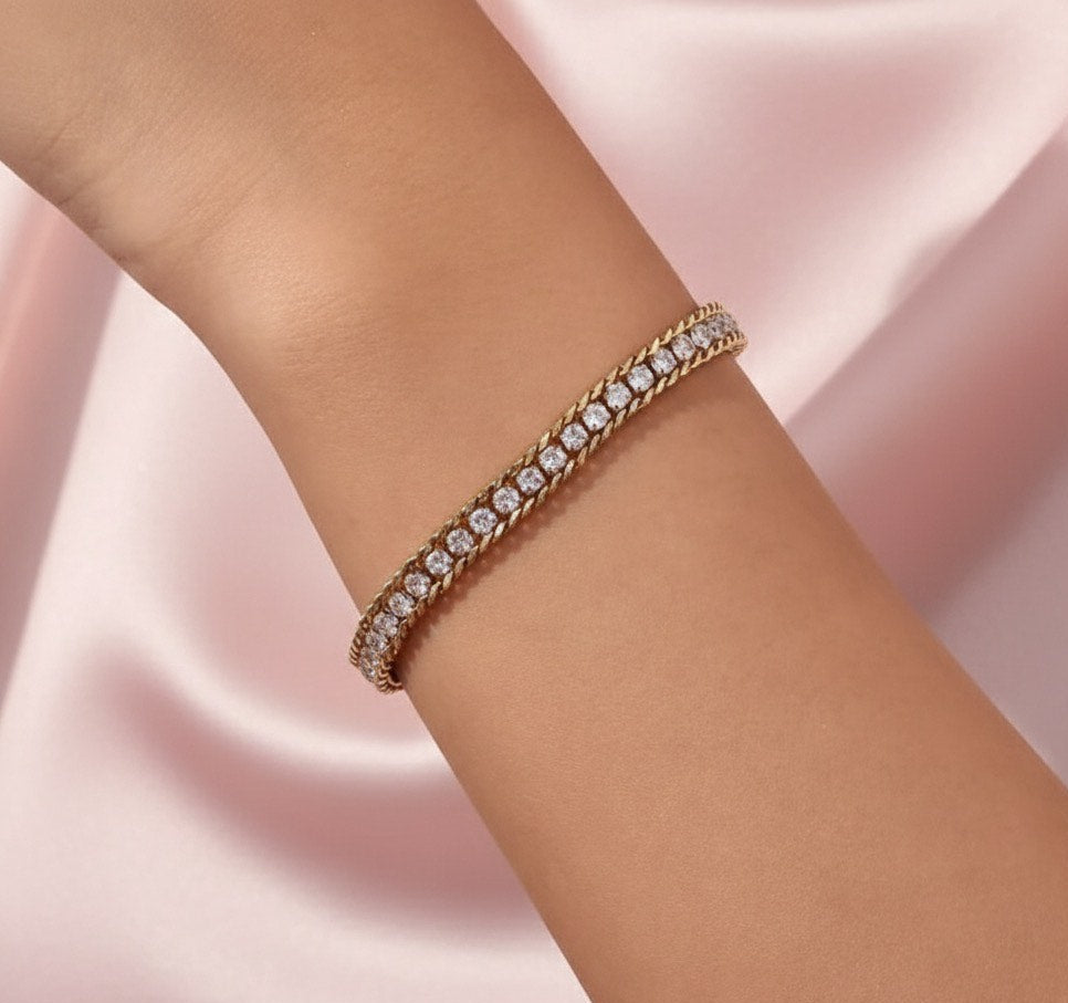 Rose gold bracelet with clear stones on a person's wrist against a pink satin background