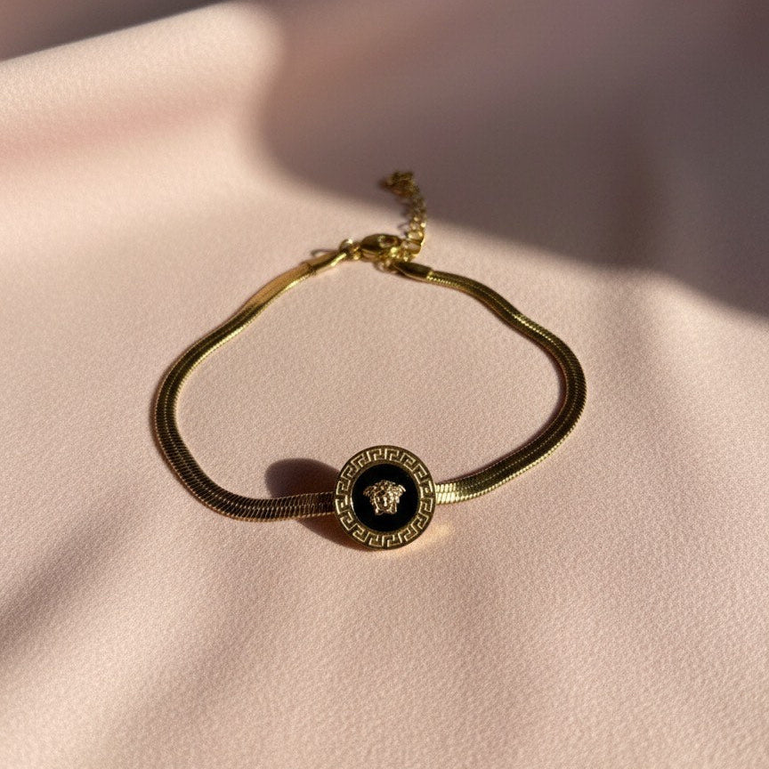 Gold bracelet with a circular emblem on a light pink surface