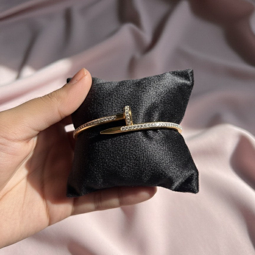 Gold bracelet on a black pillow held by a hand against a pink fabric background