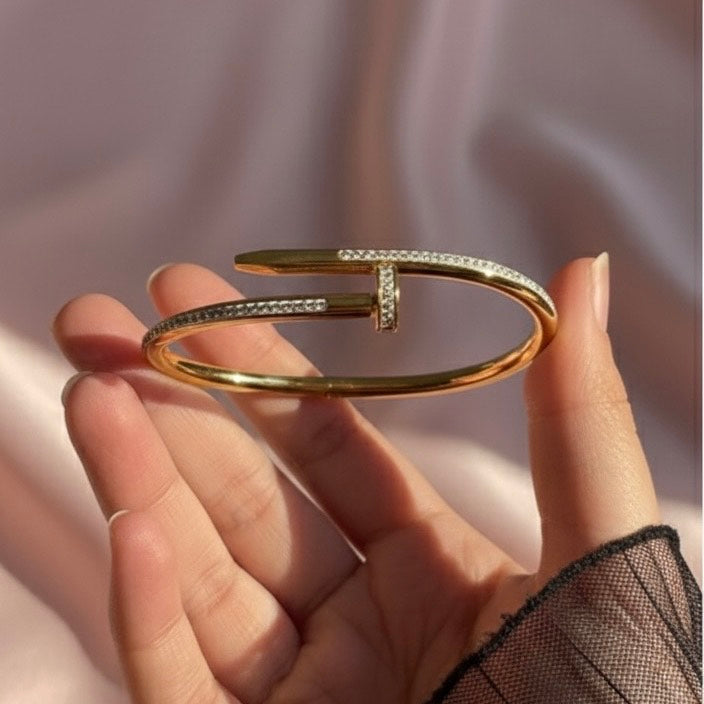 Gold bracelet held by a hand against a soft pink fabric background