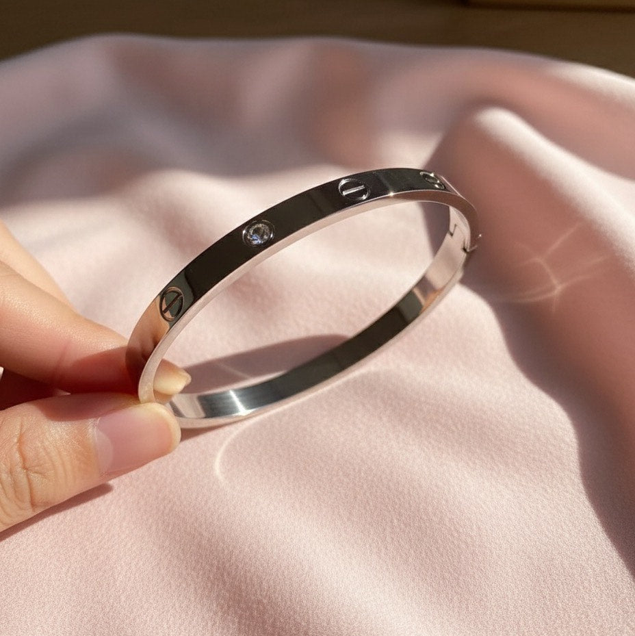 Silver bracelet with engraved text held by a hand on a pink fabric background
