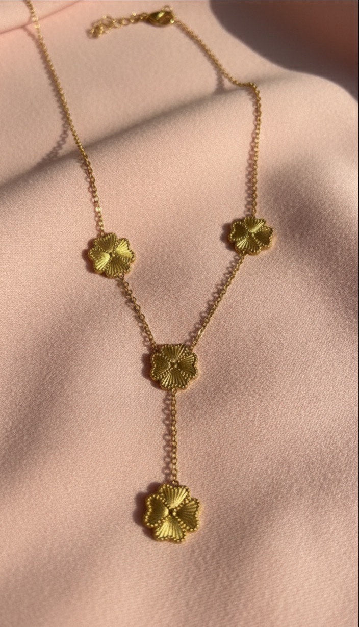 Gold necklace with floral pendants on a light pink background