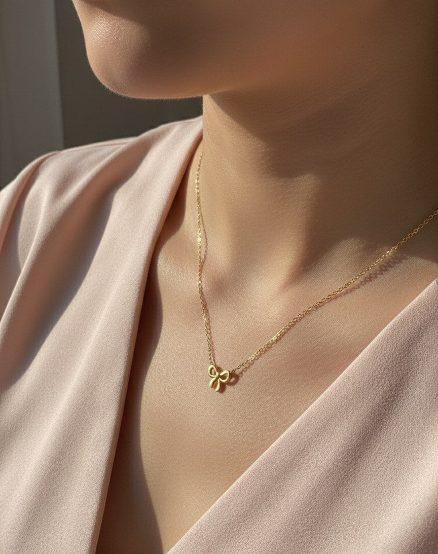 Gold necklace with a delicate pendant worn by a person in a soft pink outfit.