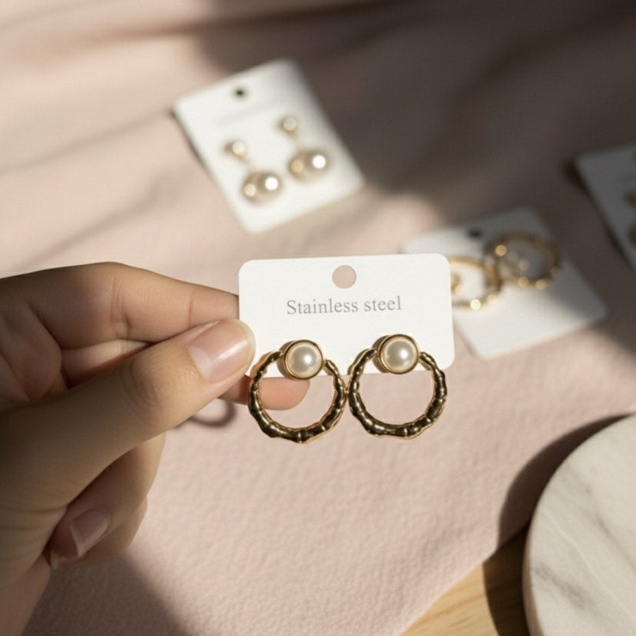 Gold hoop earrings with pearl centers held on a card, with more earrings in the background.