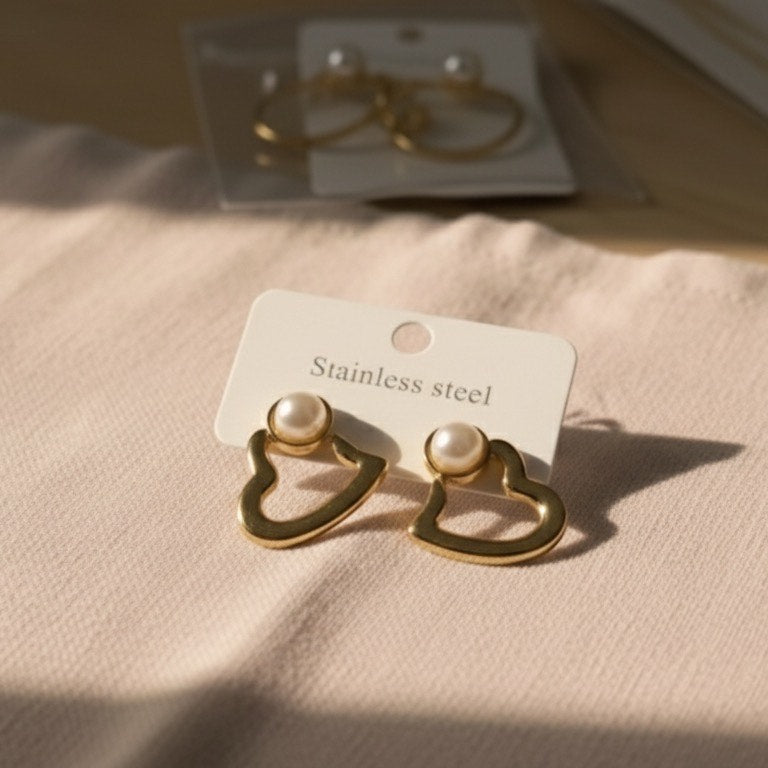Heart-shaped gold earrings on a beige fabric background with a visible brand tag.